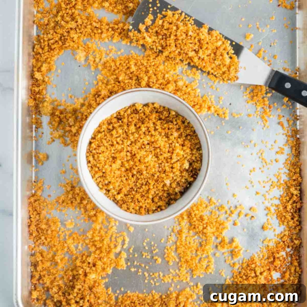 Scooping golden, crispy quinoa into a bowl with a metal spatula.