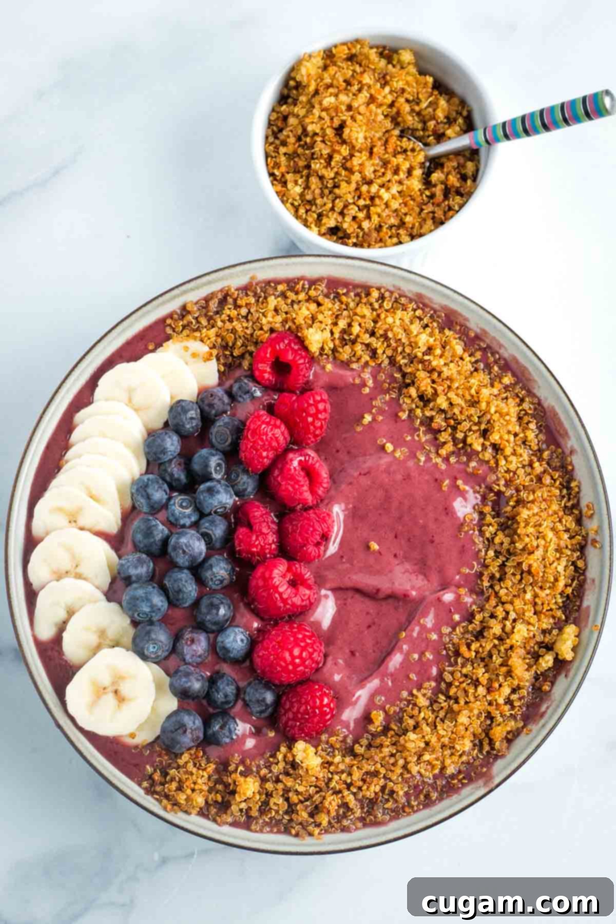 Deep purple frozen smoothie bowl topped with berries, banana slices and crispy quinoa.
