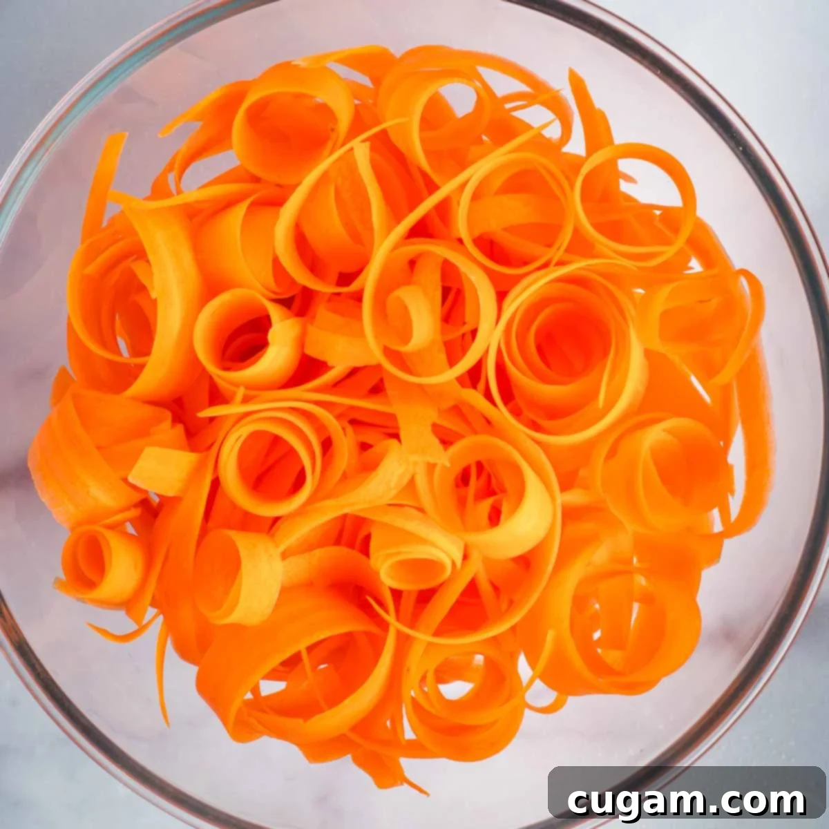 Curly ribbons of carrots piled into a mixing bowl, ready for dressing.