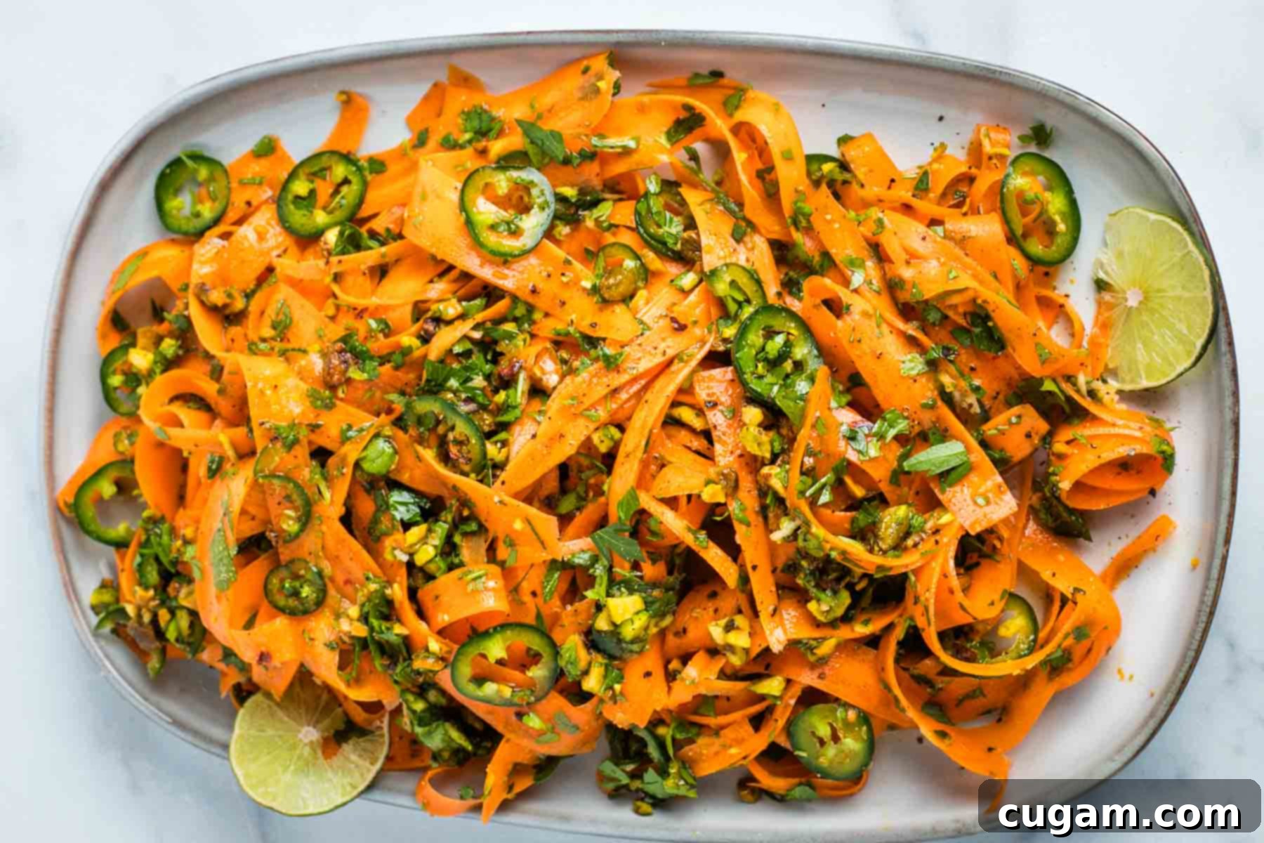 A close-up of a hand gently tossing the carrot ribbons salad with tongs, showing the glossy dressing and vibrant ingredients.