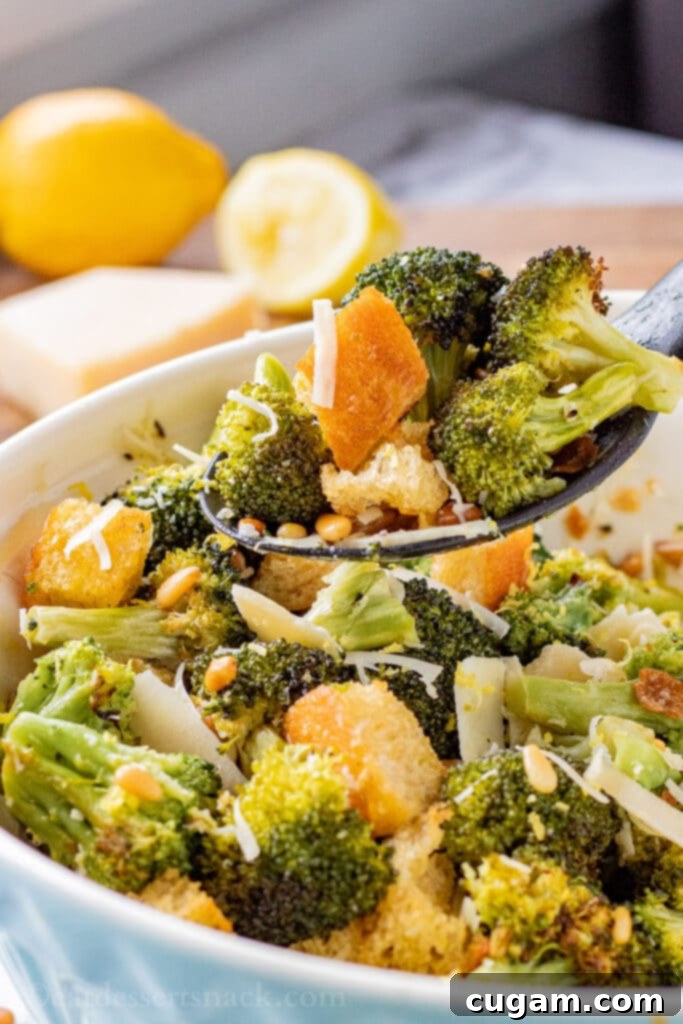 Spoonful of cooked roasted broccoli salad above blue bowl.
