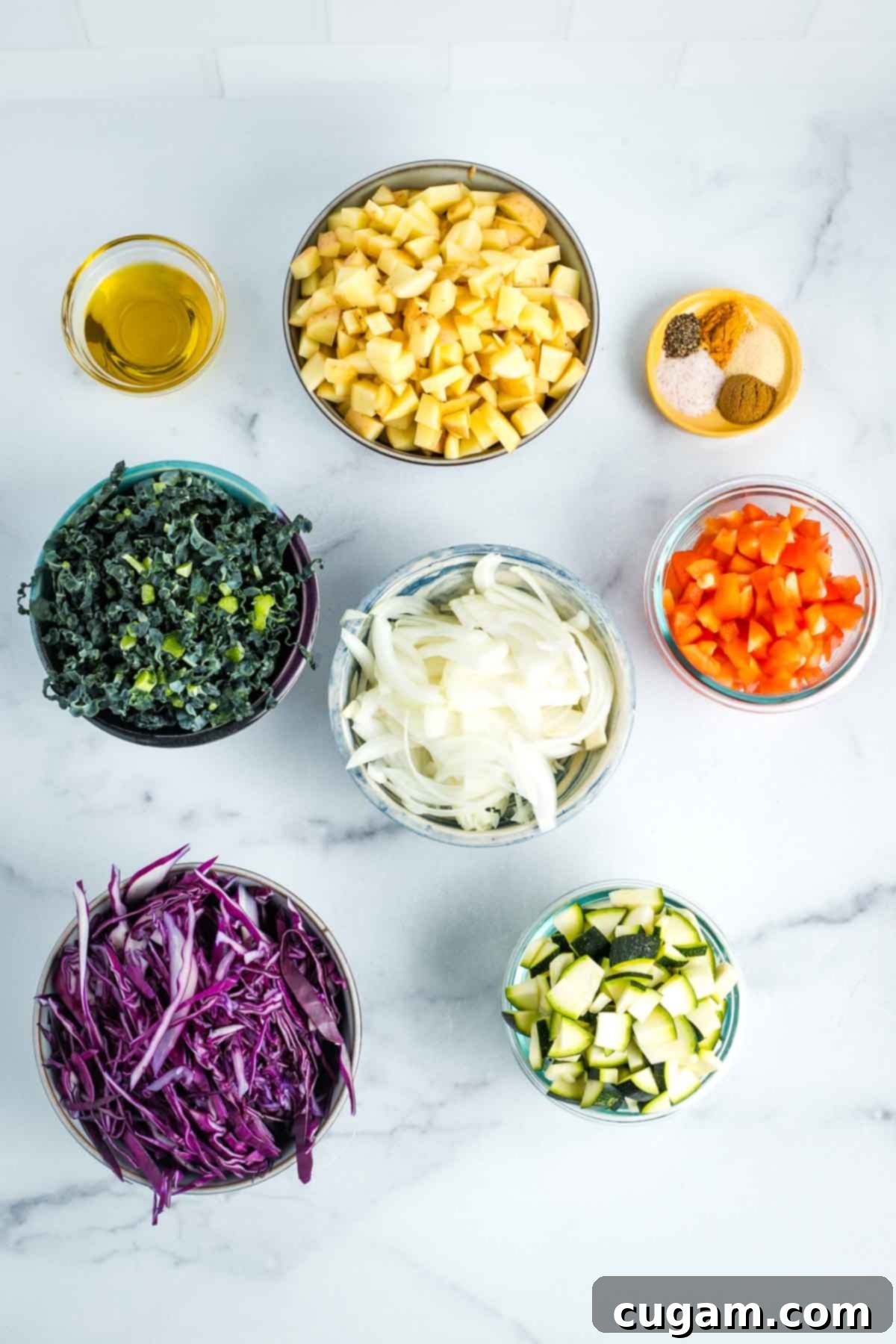 Effortless Vegan Potato and Veggie Skillet 16 Small bowls containing perfectly chopped potatoes, bell peppers, onion, cabbage, kale, and zucchini. Also shown are a dish of olive oil and an assortment of measured spices, demonstrating 'mise en place'.