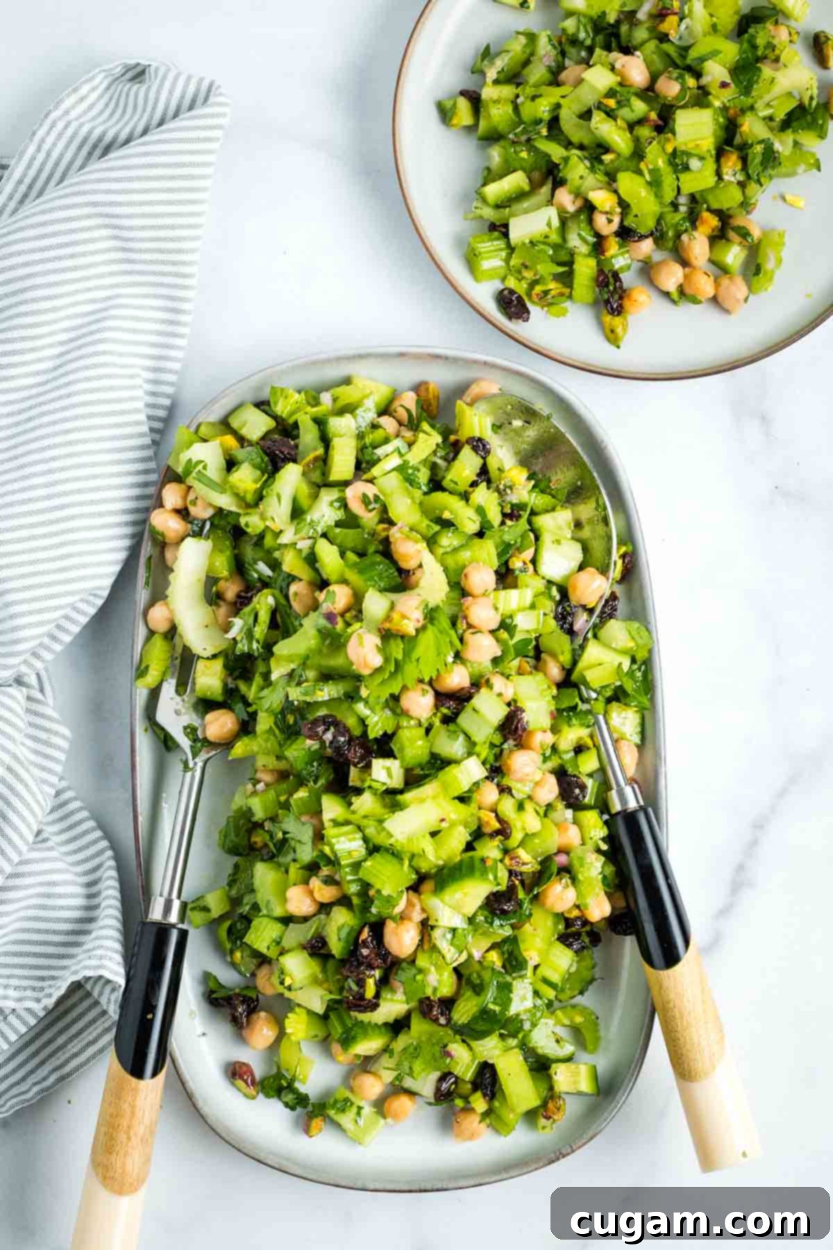 Serving a chopped celery salad with raisins, chickpeas and pistachios onto a small plate.