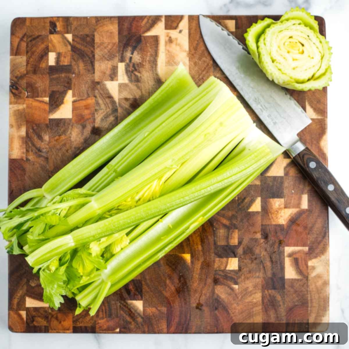 Head of celery on a wooden cutting board with the root end cut off. 