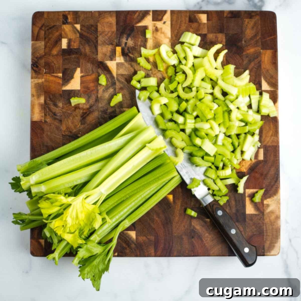 Stalks of celery, halved lengthwise, being cut across into diced pieces.