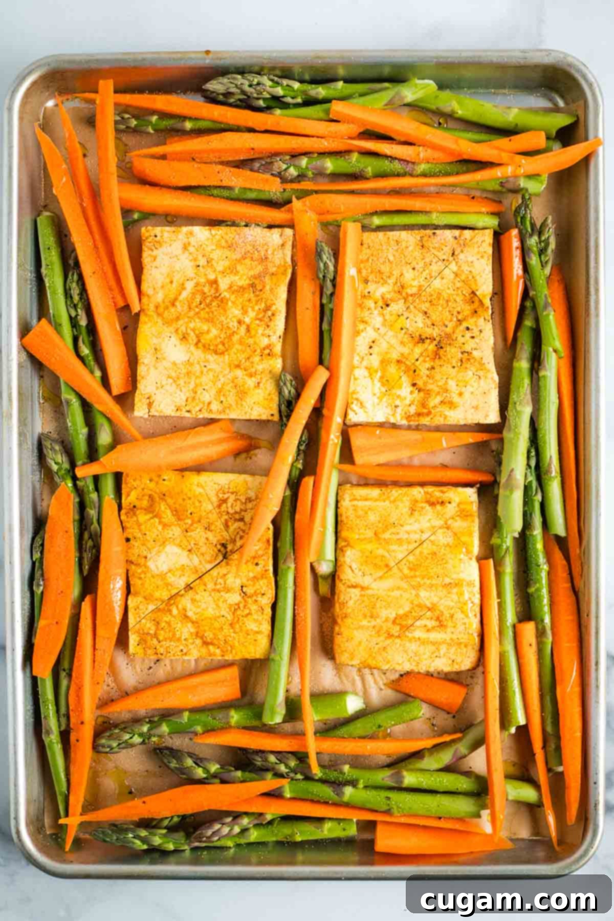 Marinated tofu steaks surrounded by carrots and asparagus on a sheet pan.