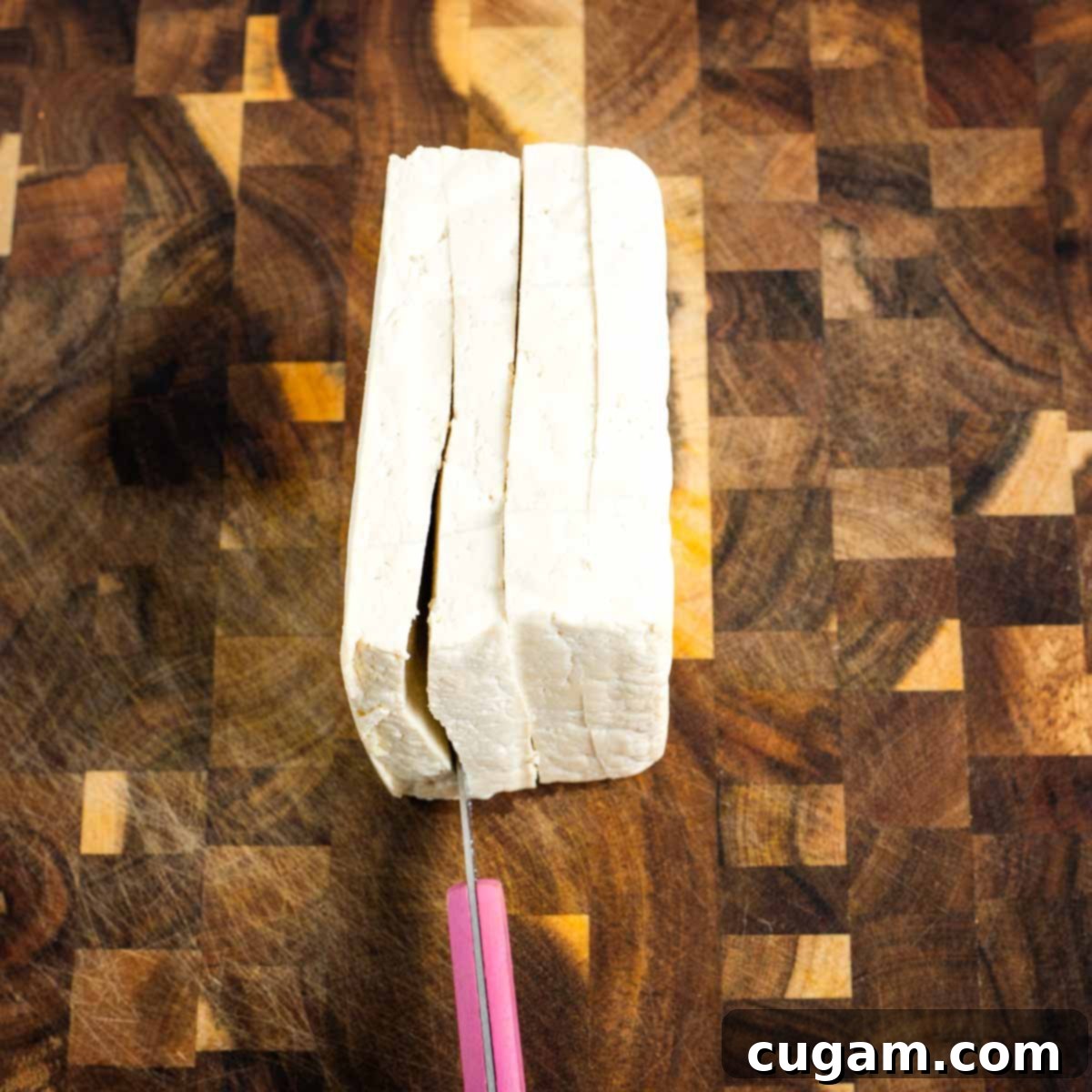 A block of tofu being cut into 4 steak slabs.