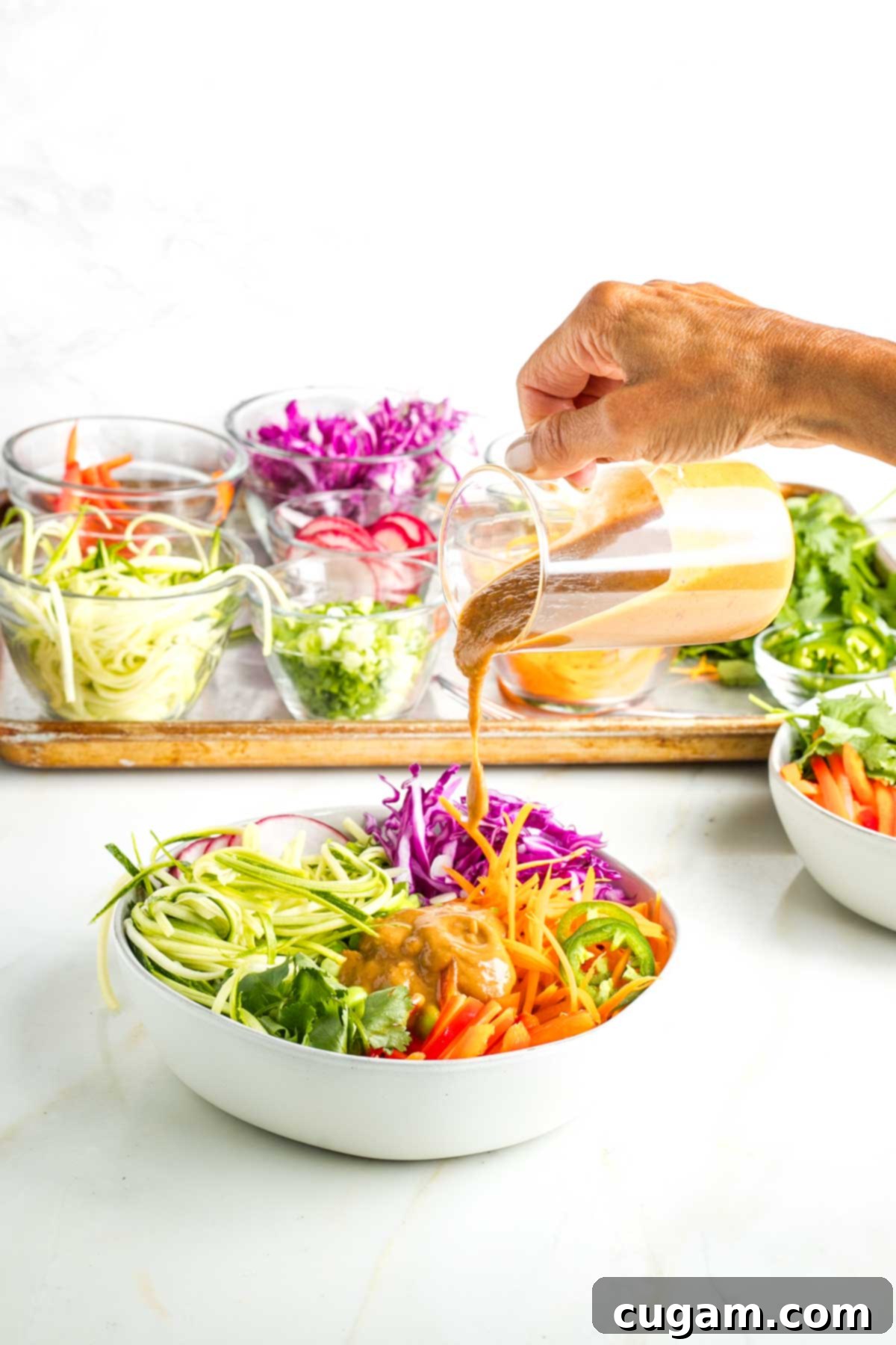 Pouring peanut sauce onto a bowl full of brightly colored veggies for a spring roll bowl.