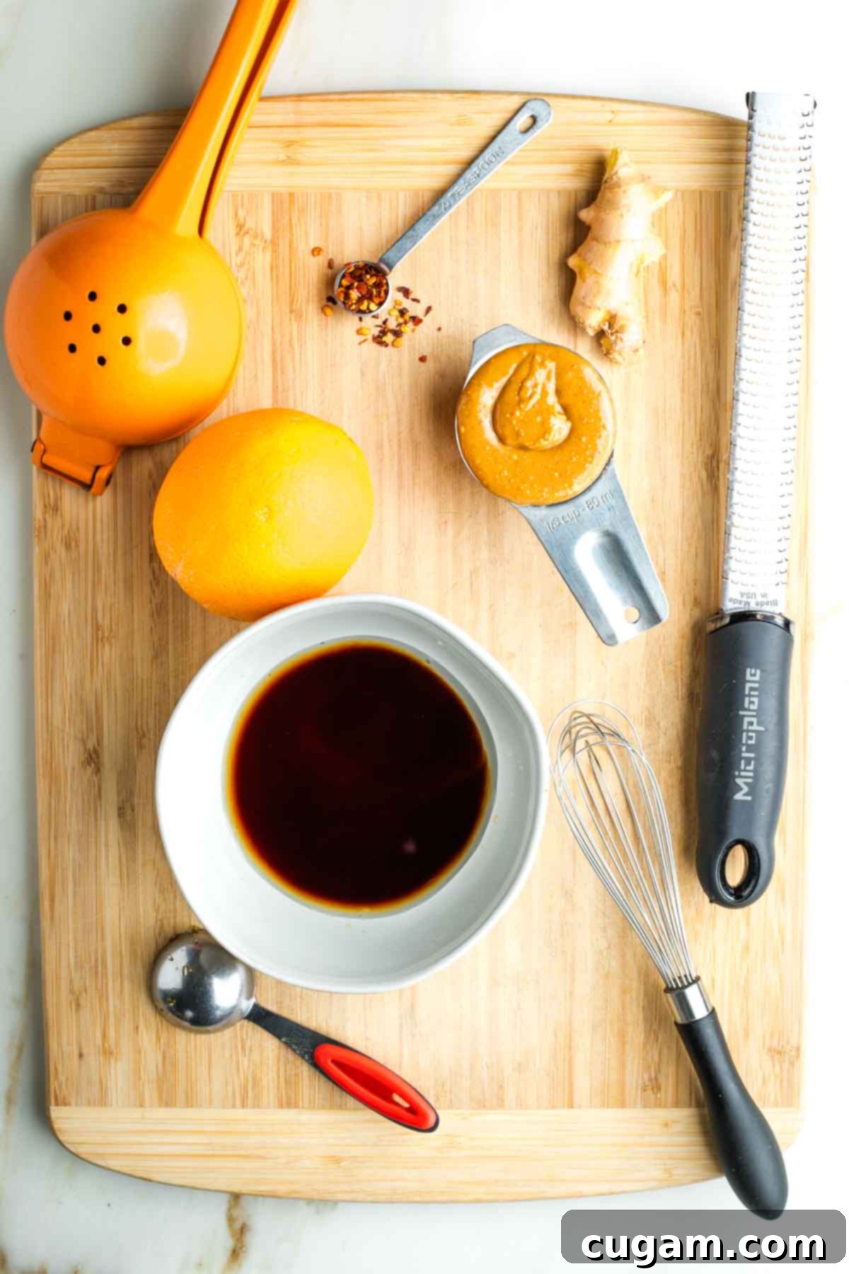 Bowl with dark liquid, plus a messy wooden board with peanut butter, zester, orange and juice squeezer.