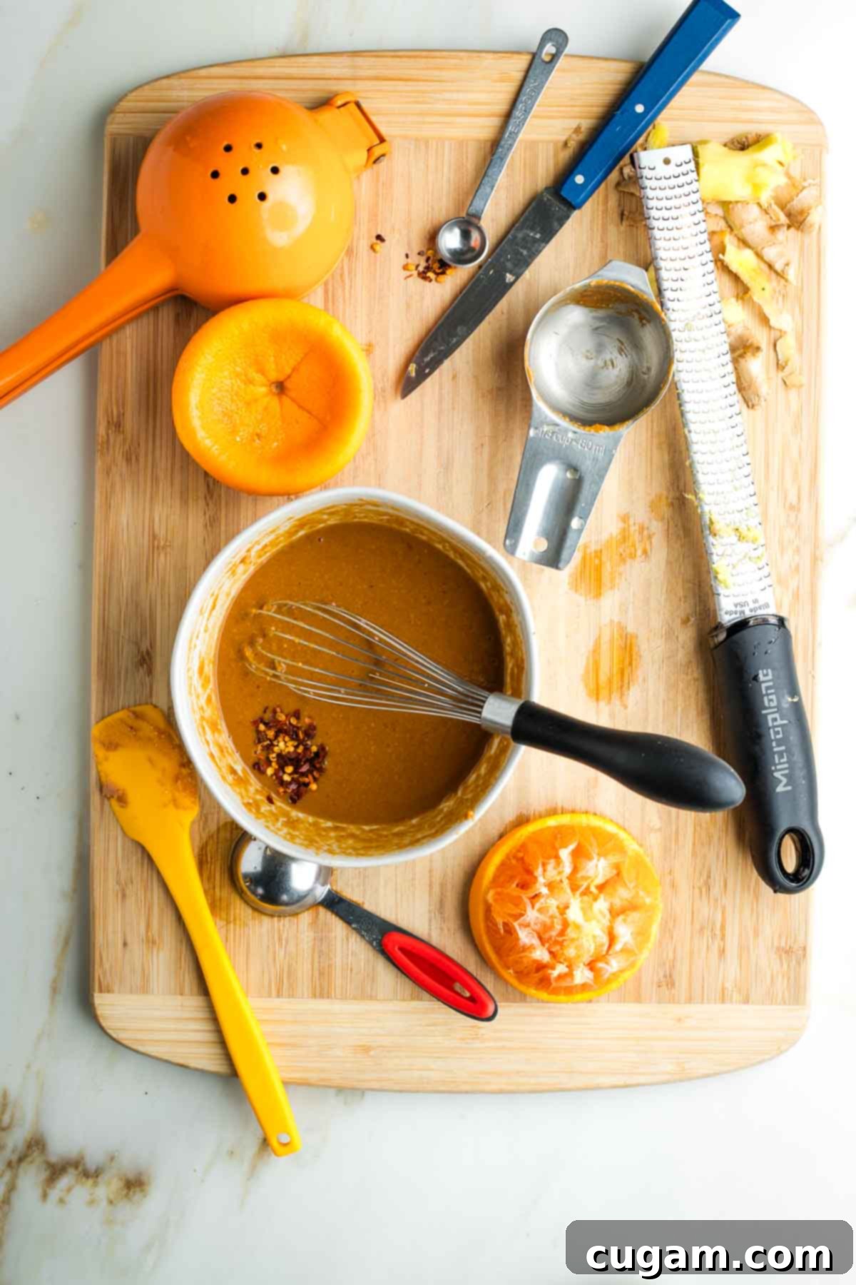 Whisking peanut sauce with crushed red pepper on a wooden board with kitchen tools.