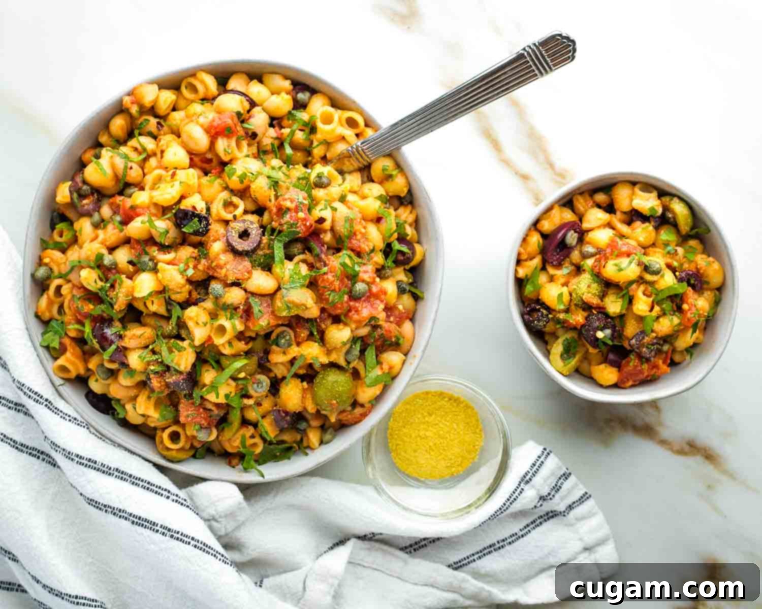 A large serving bowl and a smaller individual bowl of vegan pasta puttanesca with white beans.