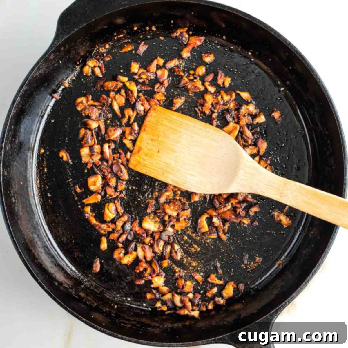 Wooden spatula pushing around diced and spiced shiitake mushrooms.