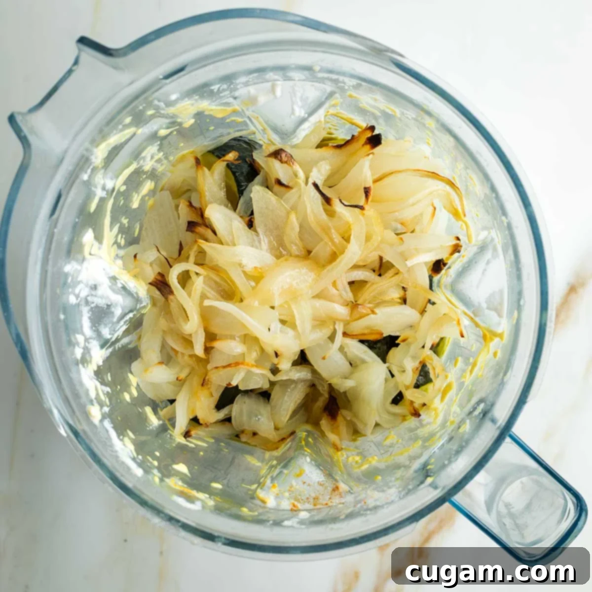 Roasted zucchini halves, tender onions, and soft garlic pulp are carefully added on top of the turmeric-infused cashew cream inside the blender, ready for the final blending stage.