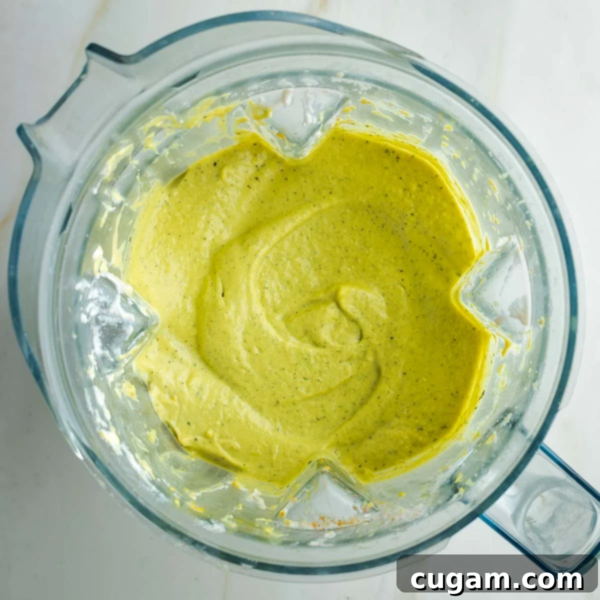 The blender pitcher now holds a thick, creamy, and subtly greenish dip, indicating a perfectly smooth and uniform texture after blending all the roasted vegetables and cashew cream.