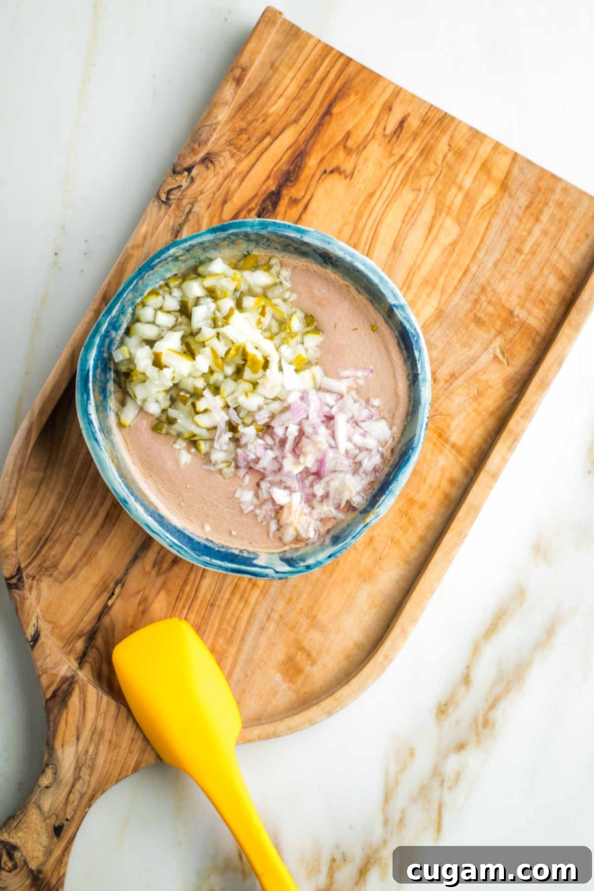 Zesty Russian Slaw 11 Diced pickles and minced shallot on top of a creamy orange dressing in a small bowl.