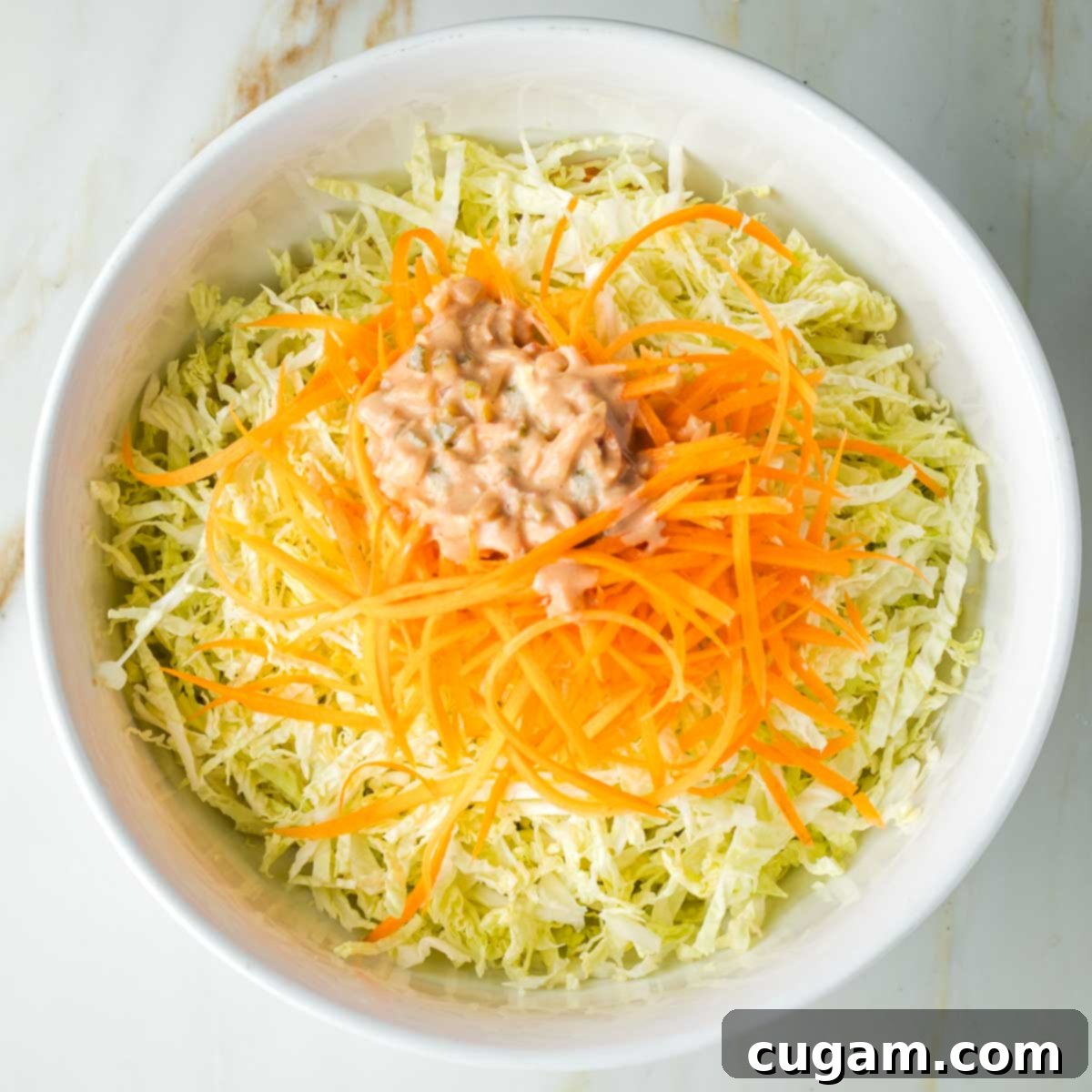 Zesty Russian Slaw 13 A pile of Russian dressing, chunky with pickles on top of a bowl of shredded cabbage and julienned carrots.
