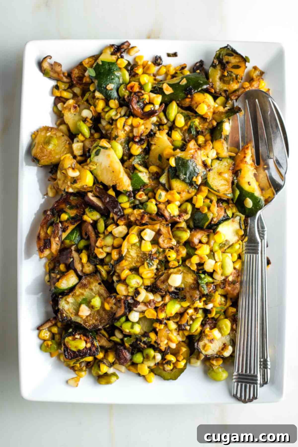 Charred zucchini and mushrooms with corn, onion and edamame in a skillet, ready to serve.