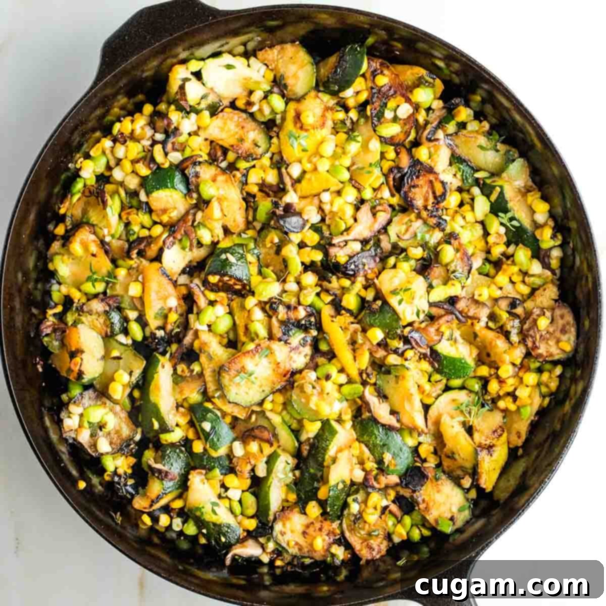 Charred zucchini, mushrooms, corn, and edamame in a cast iron skillet, sizzling and ready to be served.