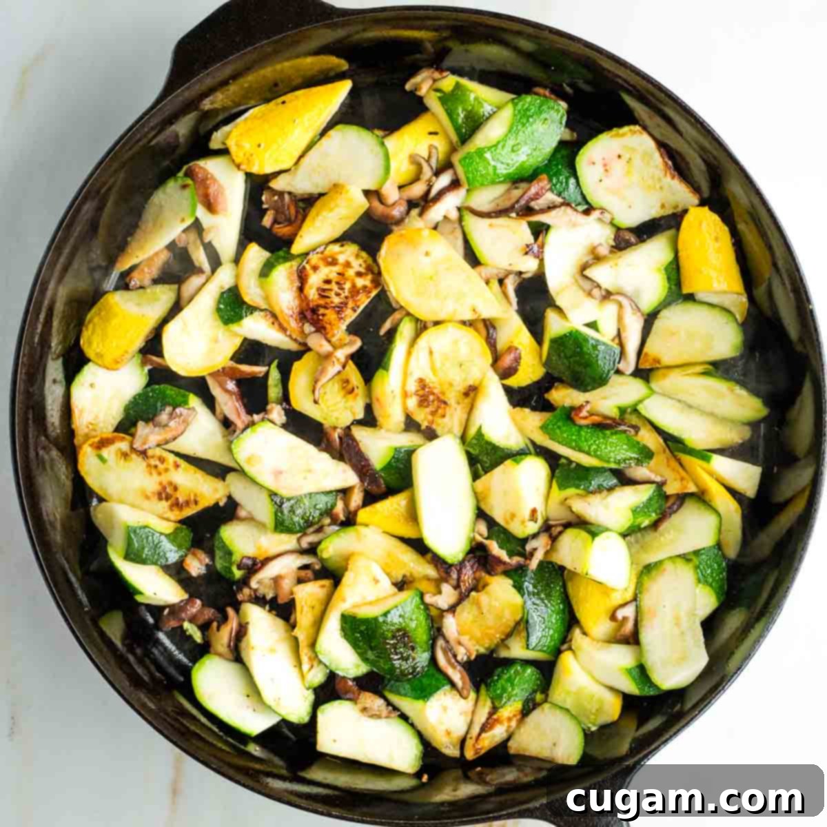 Chunks of zucchini and summer squash with mushrooms, visibly charred and caramelized in a skillet.