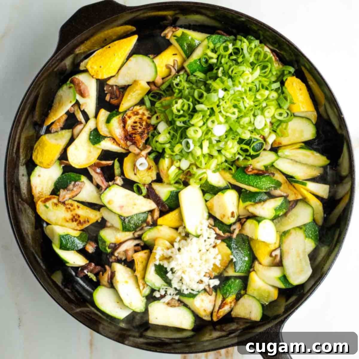 Sliced scallions and minced garlic added on top of the charred zucchini and mushrooms in the skillet.