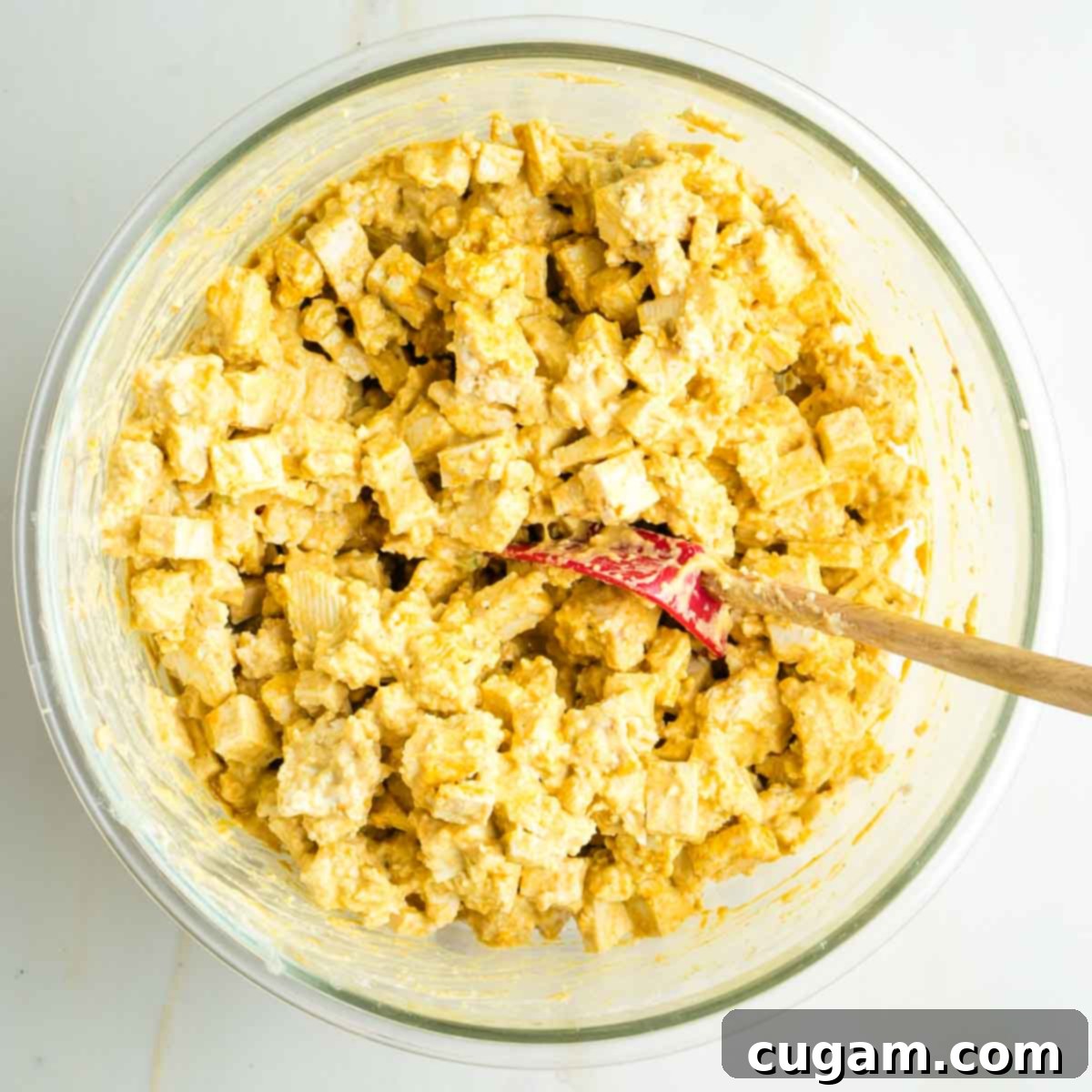 Cubes and small torn pieces of tofu mixed with creamy yellow sauce.