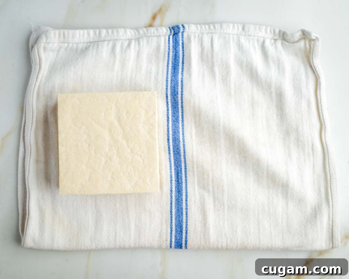 Block of tofu on a white kitchen towel with blue stripe. 