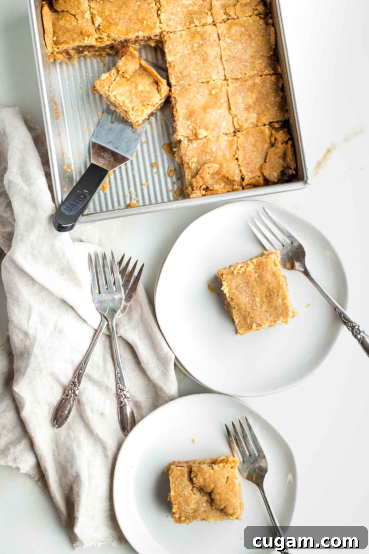 Apple pie bars on plates with forks and in the square brownie pan being served. The bars show layers of flaky crust and a rich apple filling.