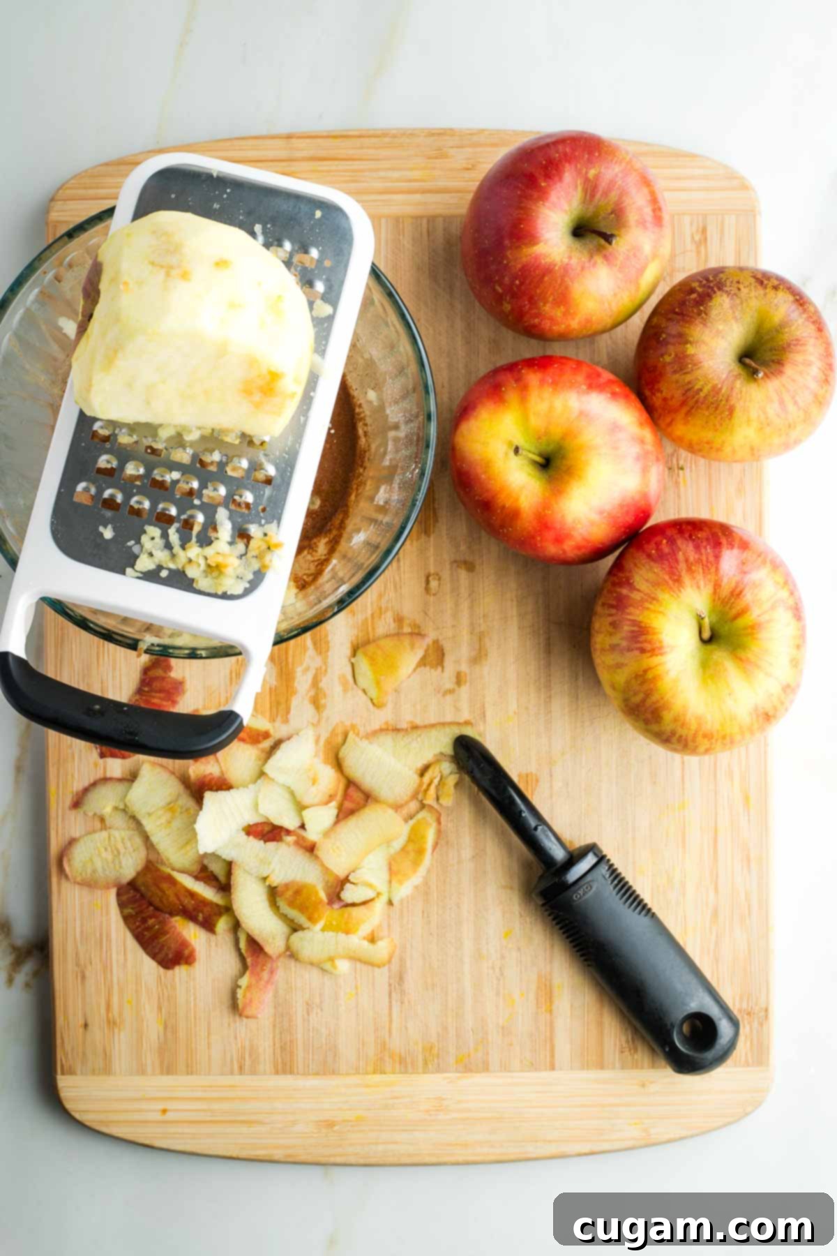 Apples, and apple peels, plus a peeled apple being grated directly into a glass bowl with the spice mixture.