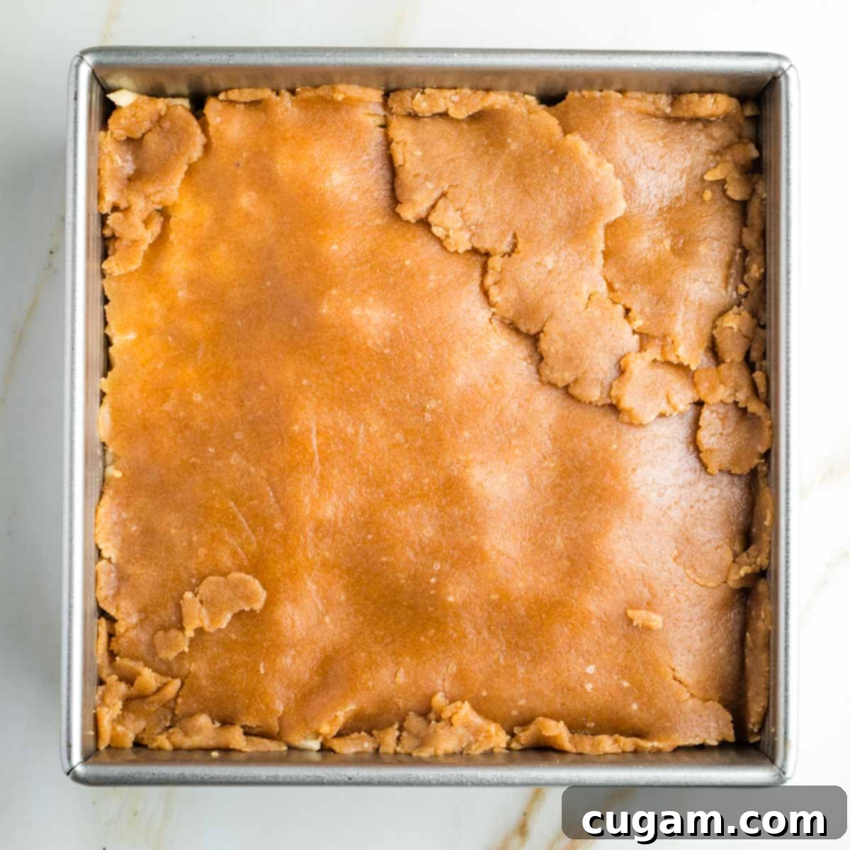 Pie dough pieced together, covering the apples in a square pan, ready for baking.