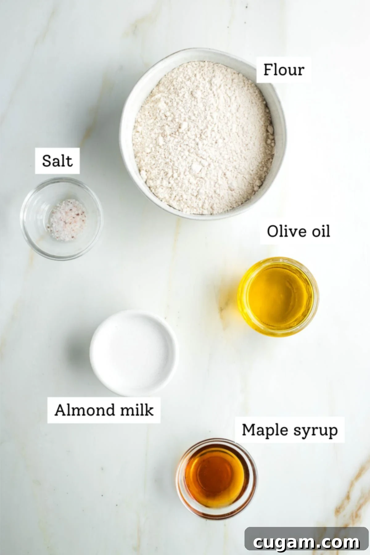 Labeled ingredients for vegan pie crust: flour, salt, olive oil, almond milk and maple syrup on a dark background.