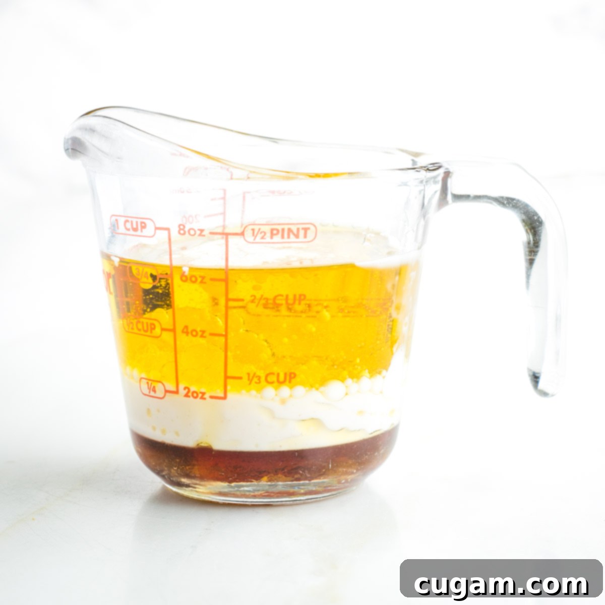 Pyrex measuring cup with olive oil, almond milk and maple syrup. The liquids are clearly separated before mixing.