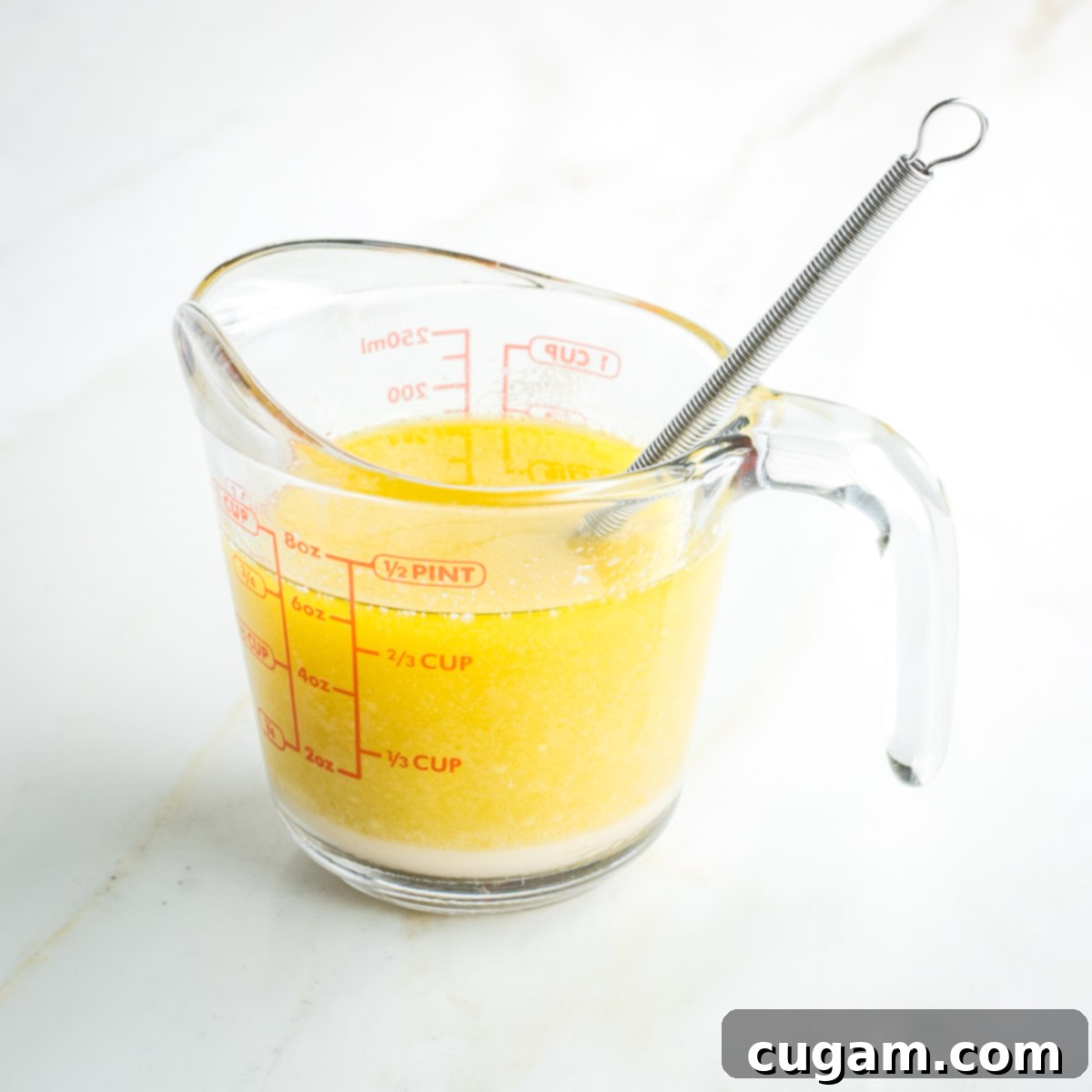 Whisk inside a one cup pyrex measuring cup filled with yellow liquid, indicating the emulsified mixture.