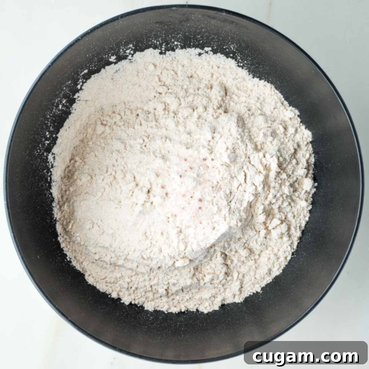 Flour and salt in a black bowl, aerated with a fork.