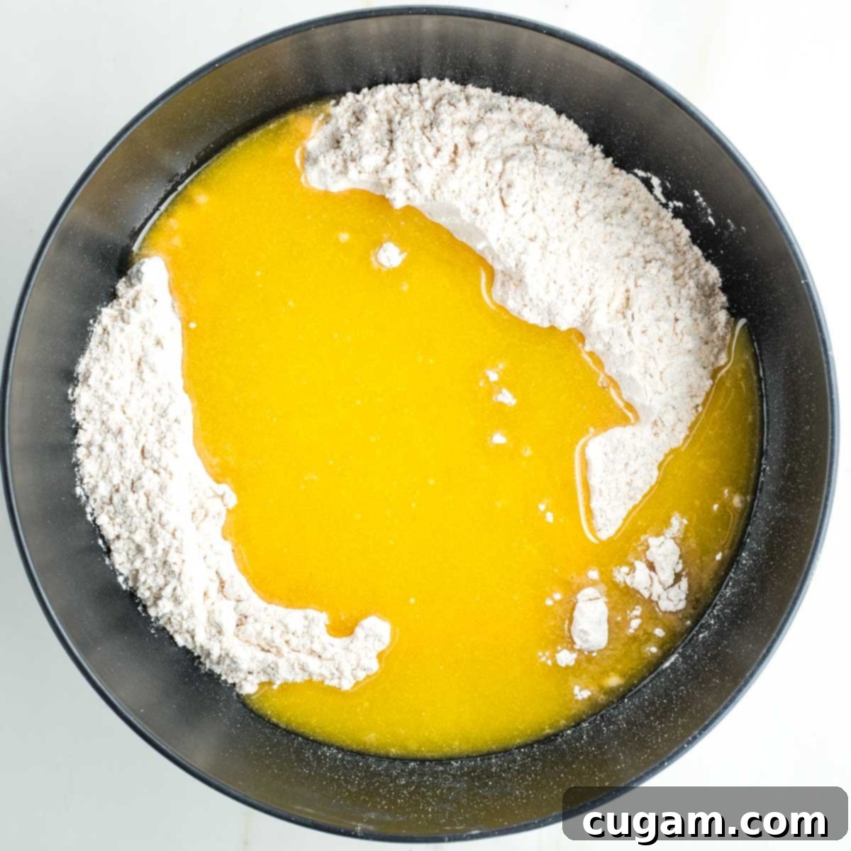 Flour in a black bowl, with the yellow liquid mixture poured on top.
