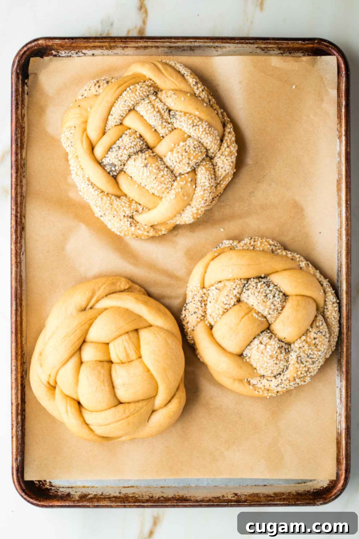 Golden Sweet Round Challah 40 Large, fluffy, round, braided loaves of unbaked challah bread on a parchment lined rimmed baking tray.