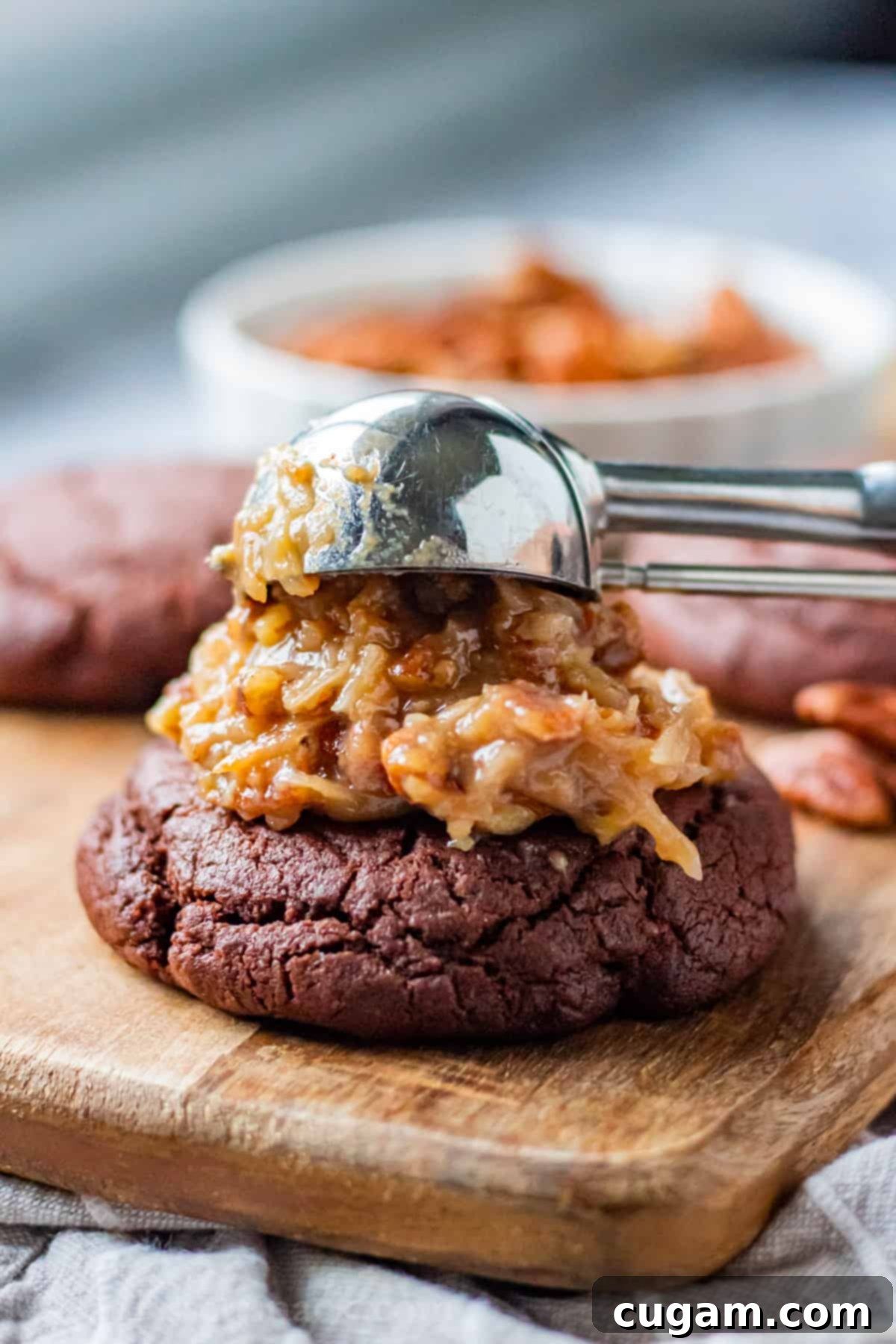 Scooping coconut pecan frosting onto baked chocolate cookie. 