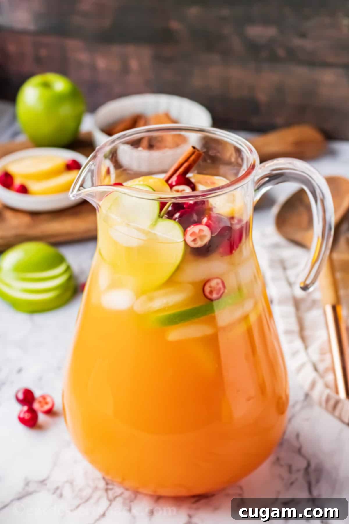 Full pitcher of apple cider punch with garnishes on a rustic background.