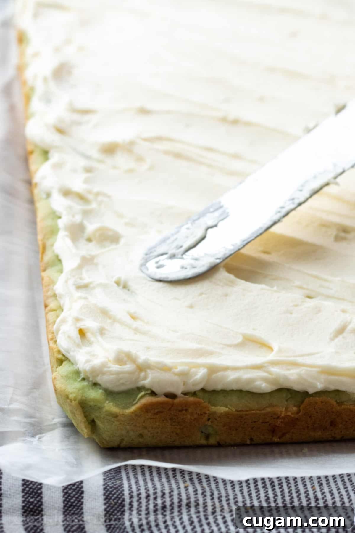 Spatula spreading frosting over baked pistachio bars. 
