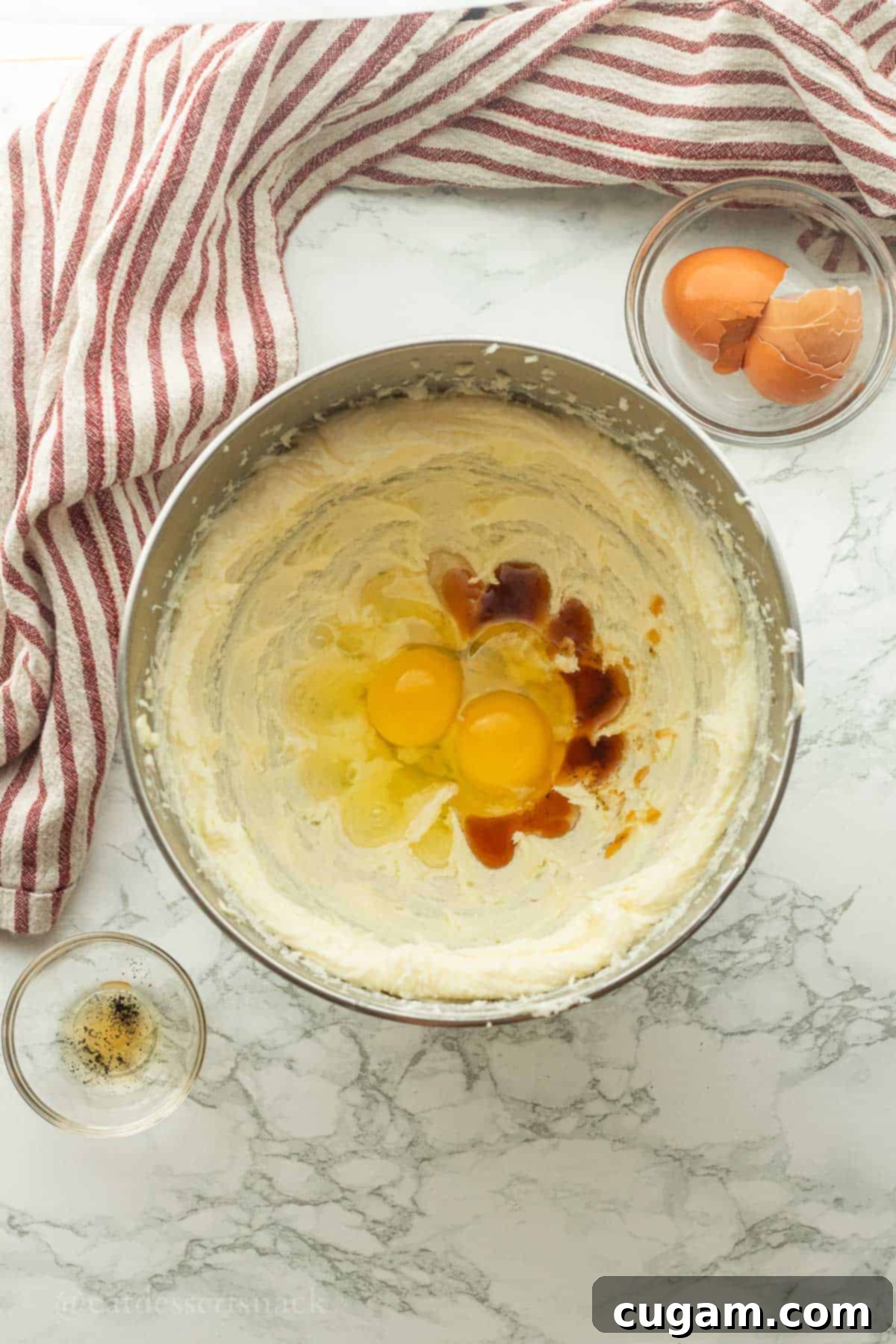 Eggs and vanilla in metal mixing bowl of creamed butter and sugar.