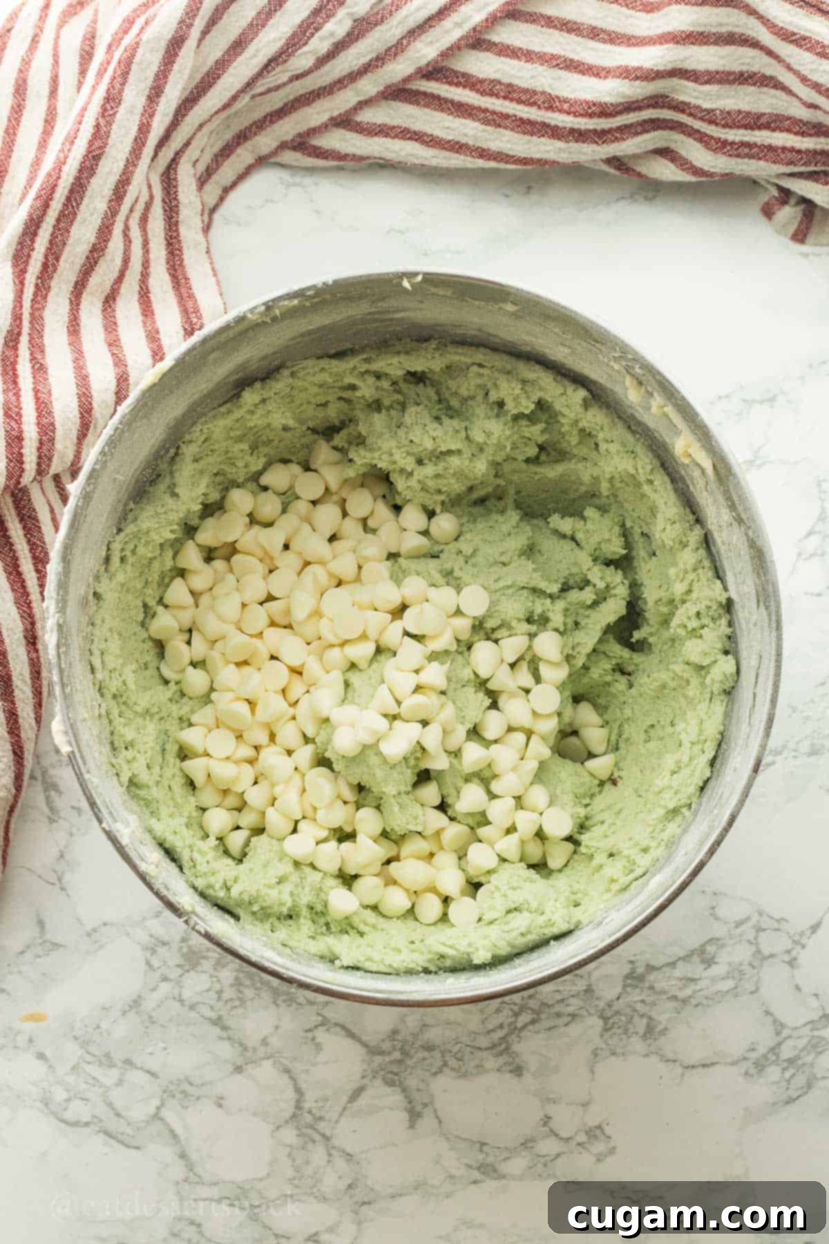 Raw pistachio bar dough with white chocolate chips in metal mixing bowl.