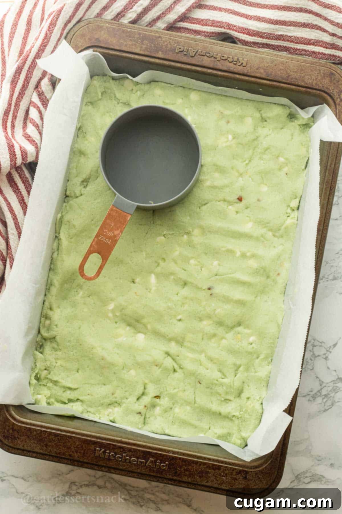 Raw pistachio bar dough in metal pan lined with parchment paper.