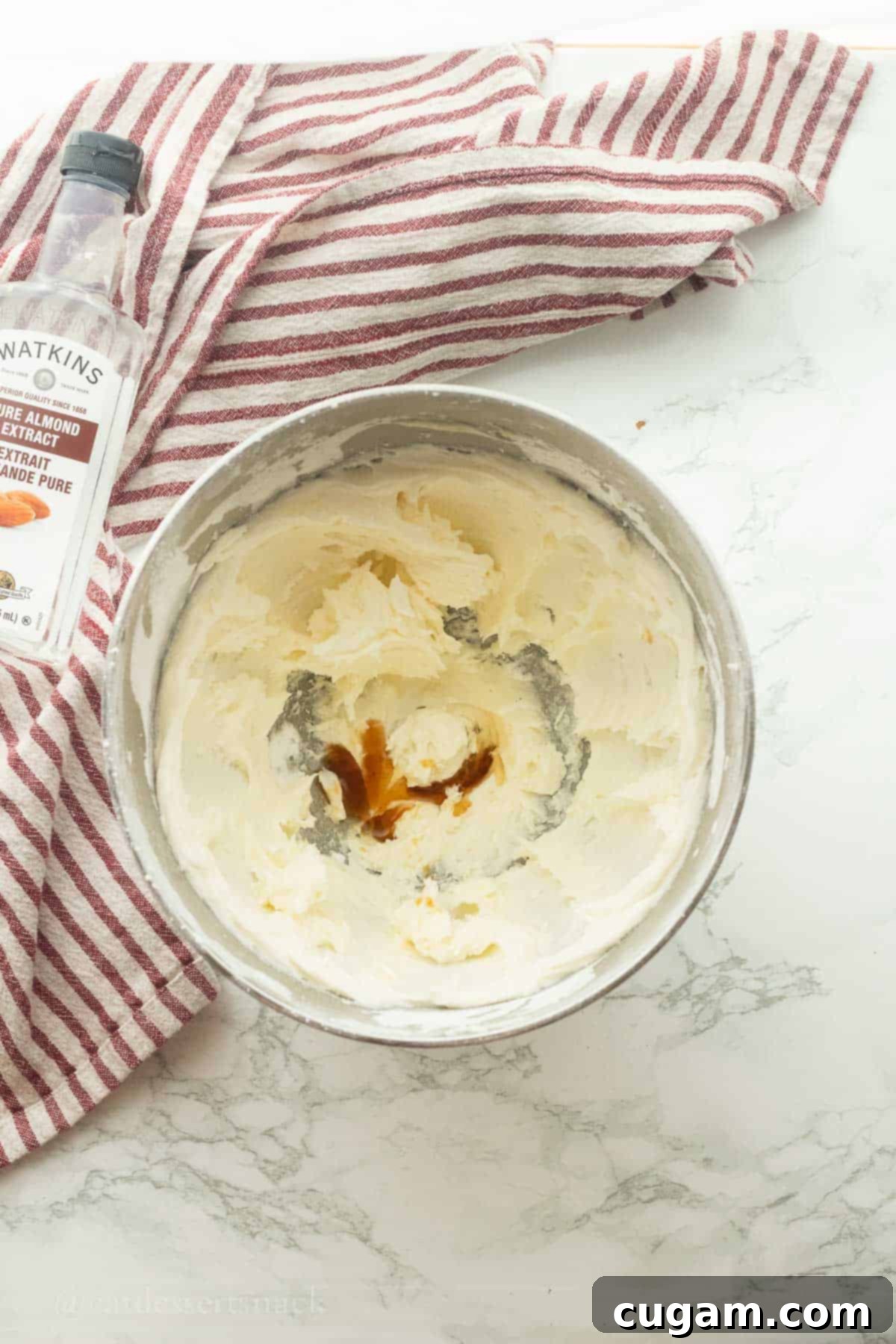Powdered sugar and butter with vanilla and almond extract in mixing bowl.