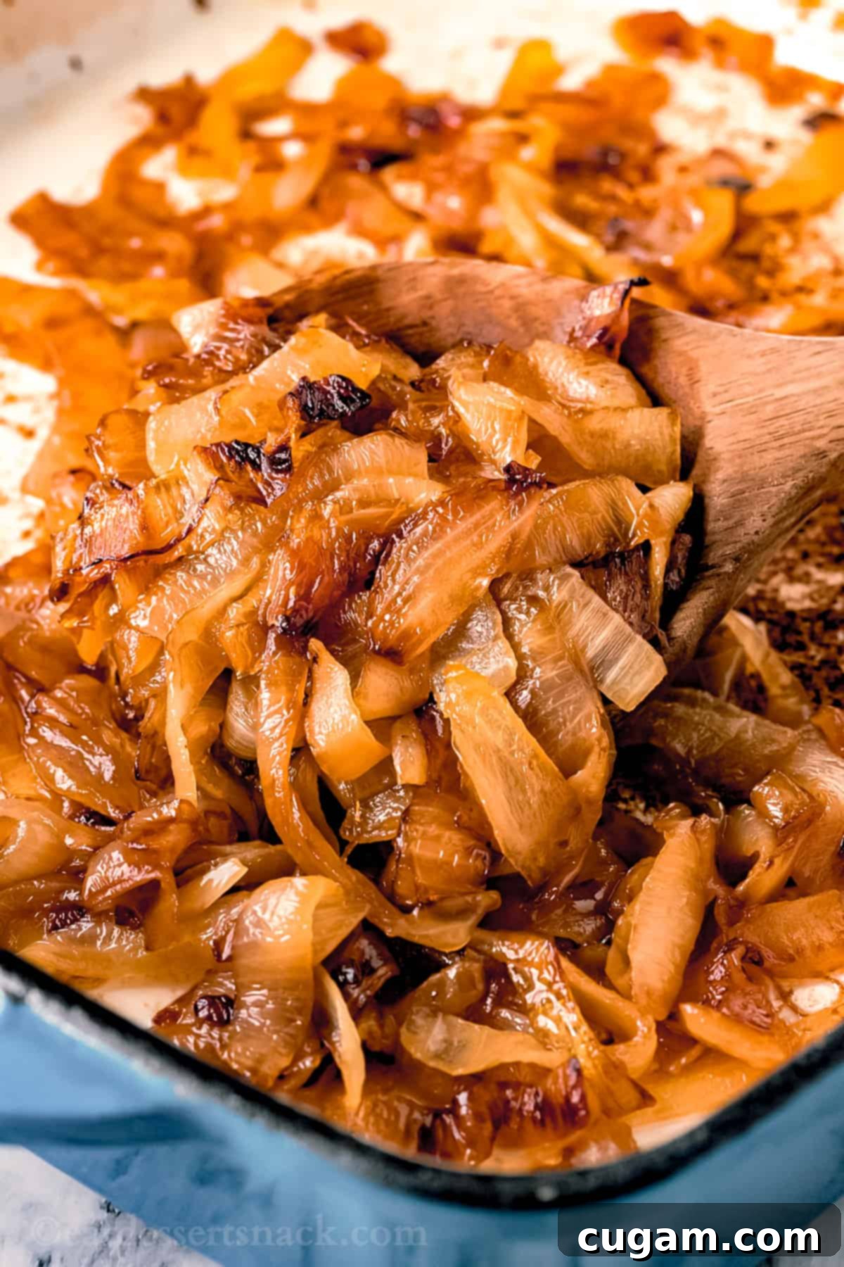 Cooked onions with wooden spoon in blue pan. 