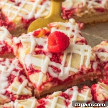 Close up view of a perfectly sliced raspberry cream bar on a gold spatula, showcasing the layers and fresh raspberries.