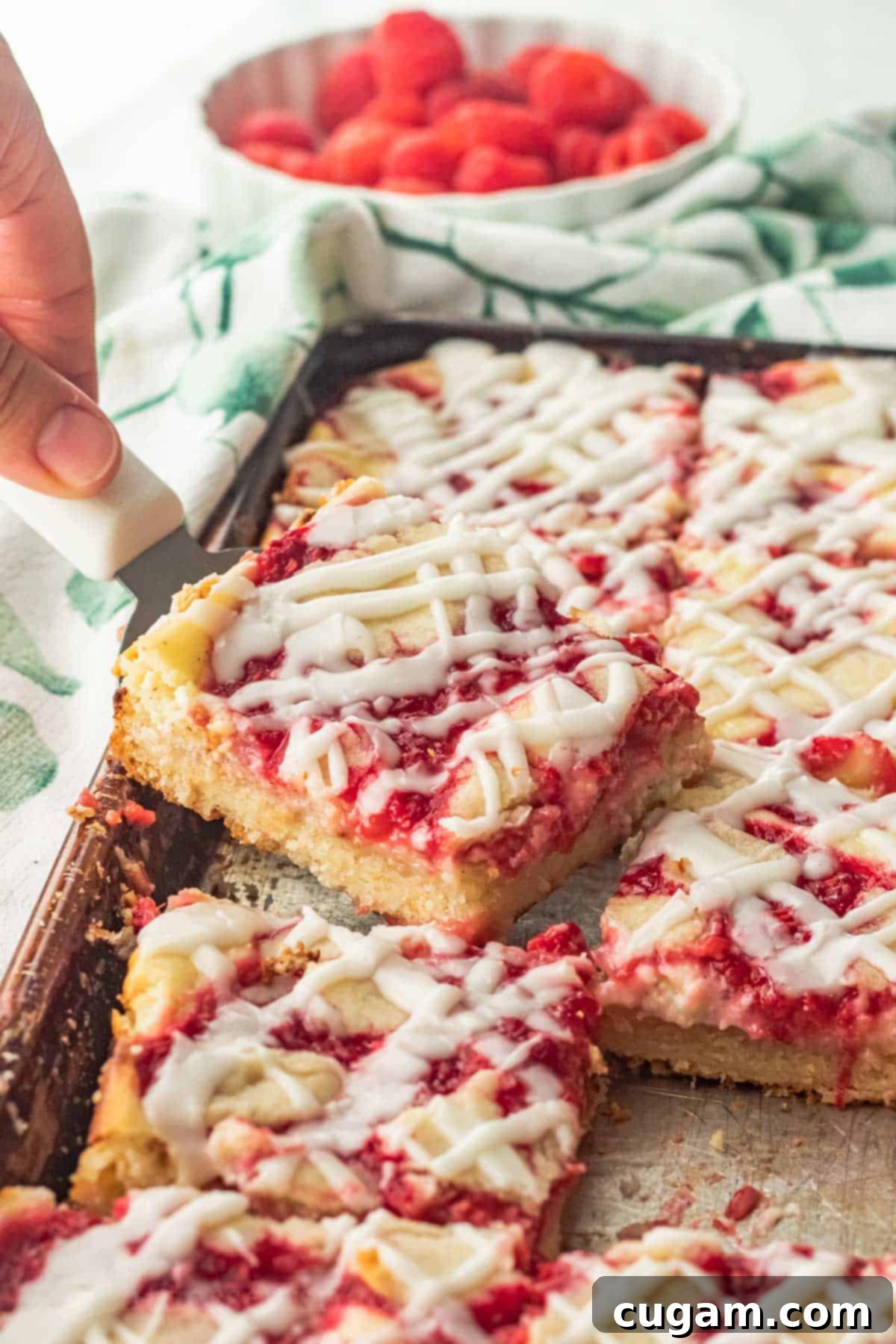 Side view of a perfectly sliced raspberry and cream bar on a metal pan of freshly baked bars, showcasing the distinct layers of crust, cream cheese, and raspberry swirls.