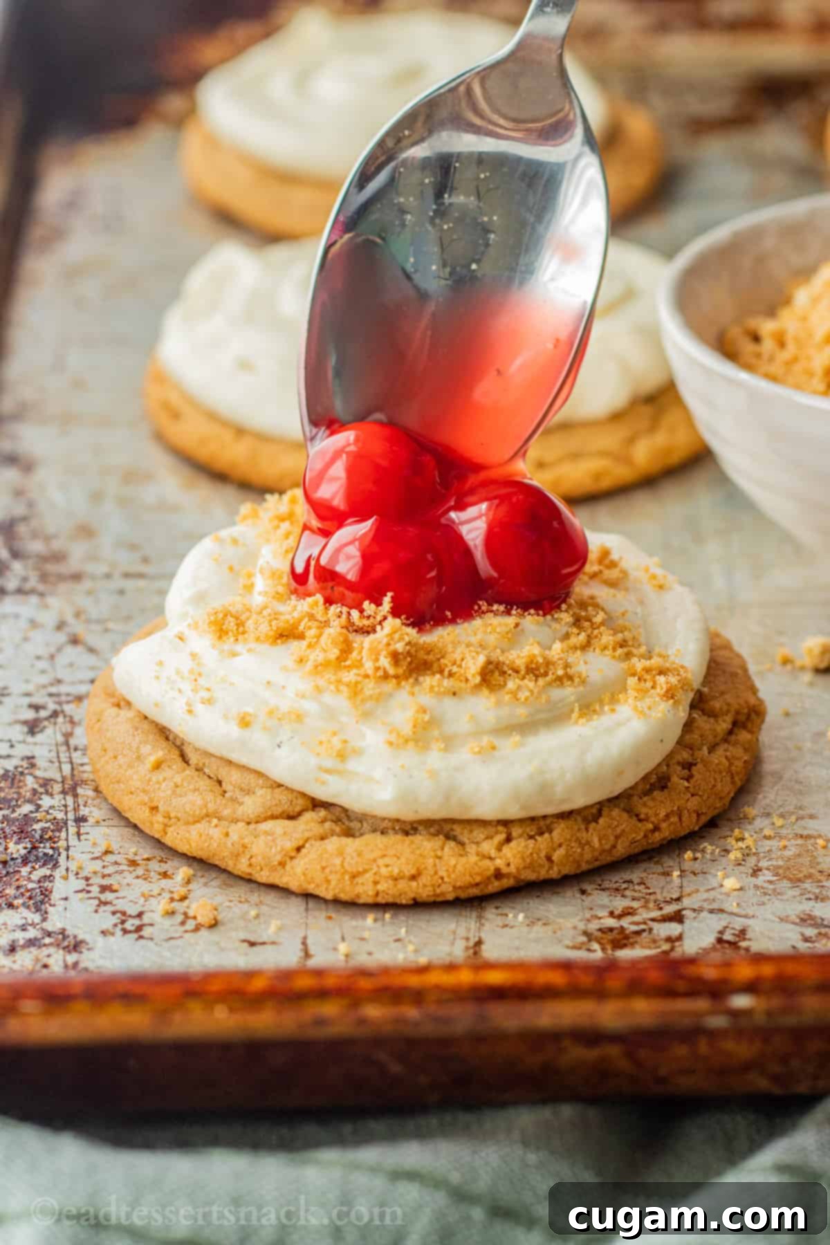 Spooning cherry pie filling onto baked cheesecake cookie. 