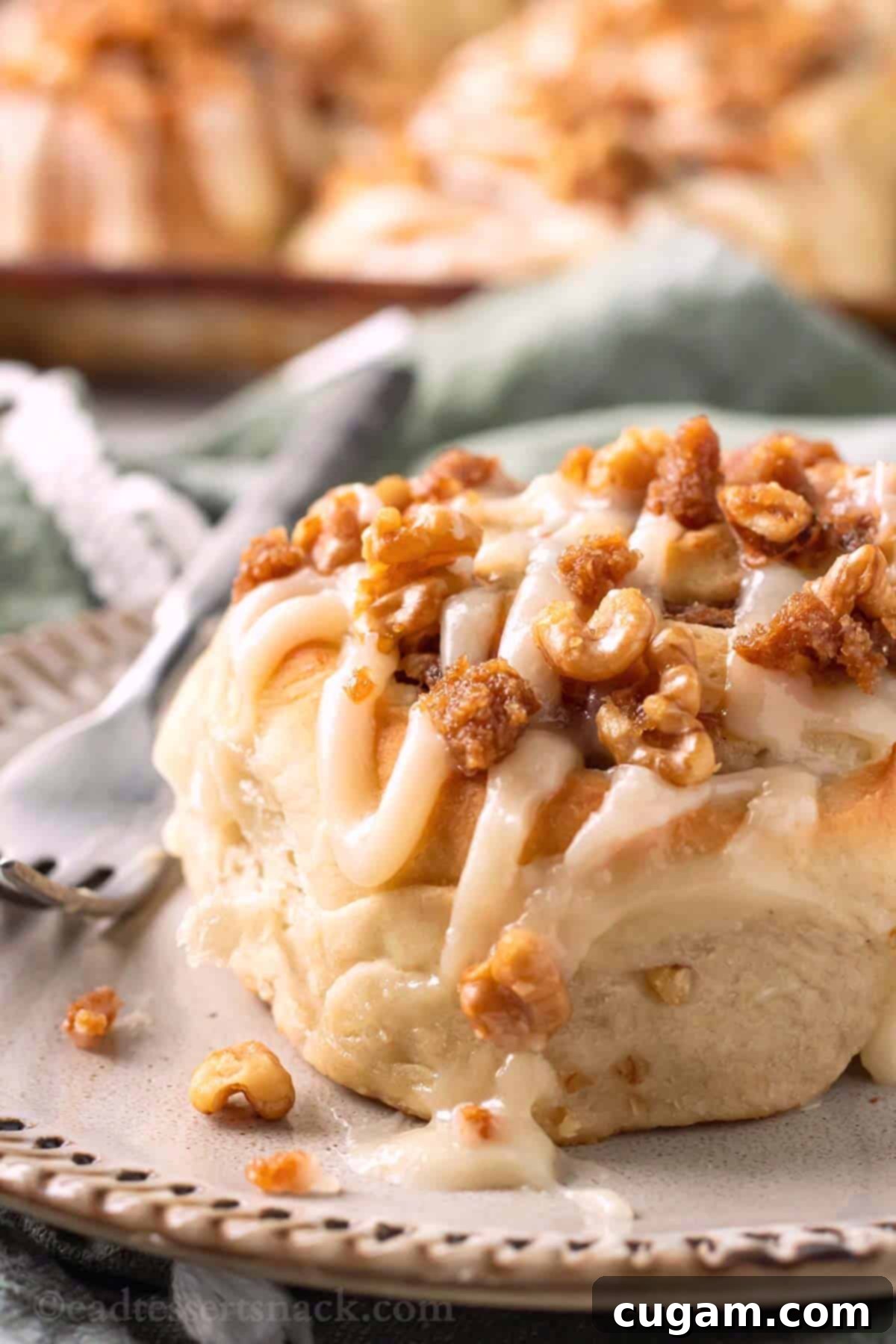 A freshly frosted banana cinnamon roll sits invitingly on a white plate, ready to be enjoyed with a fork.