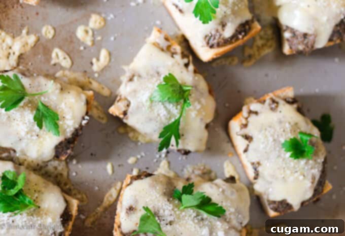 Mushroom pesto toasts topped with melted cheese and fresh parsley, resting on a silver baking sheet.