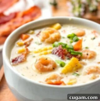 White bowl of shrimp corn chowder on wood plate.