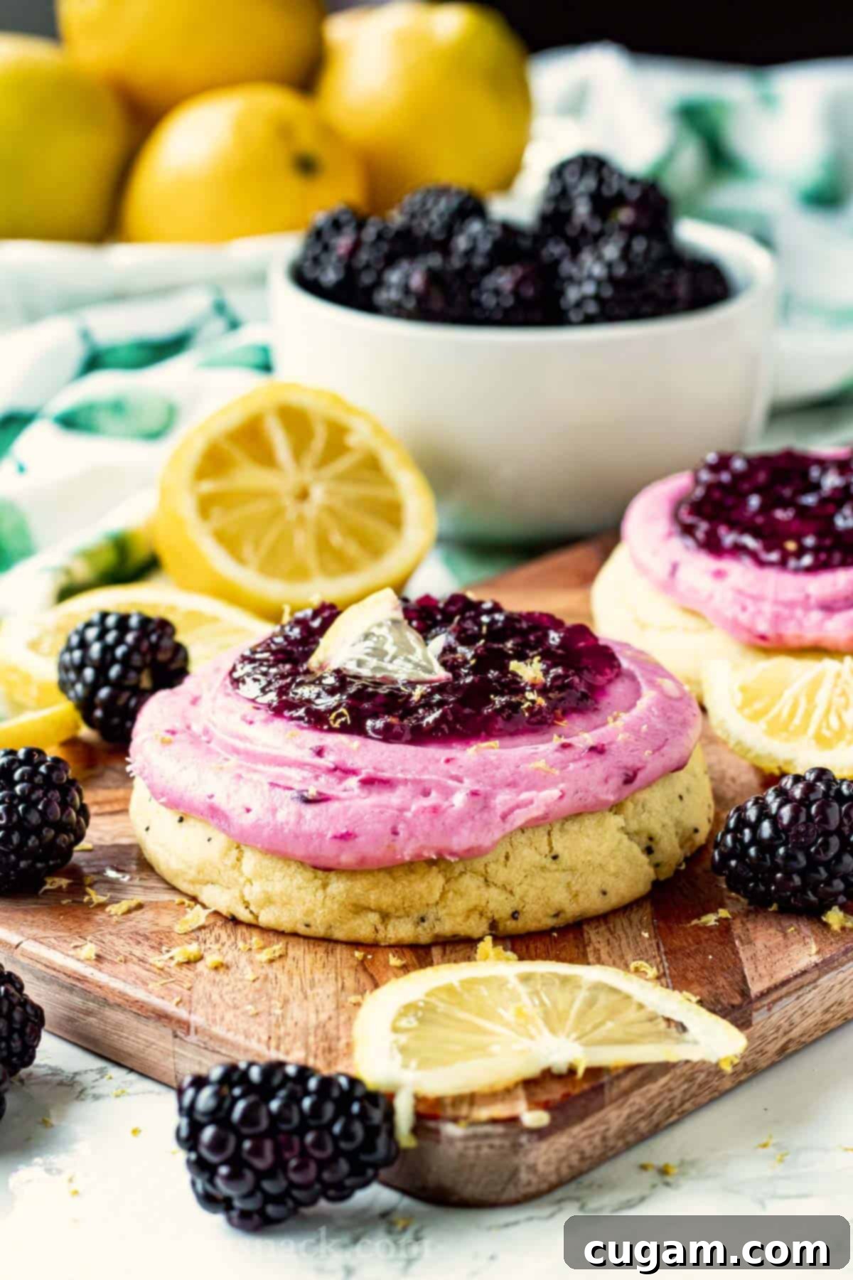 Baked Lemon Blackberry Cookie with frosting on wooden cutting board with lemon slices and blackberries. 